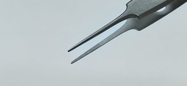 A Bishop-Harmon dressing forcep on a gray background.
